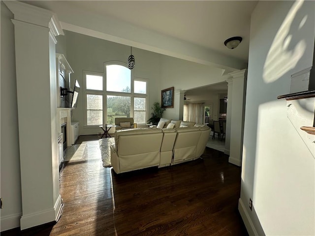 living area with baseboards, a fireplace with flush hearth, dark wood-type flooring, and ornate columns