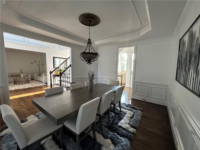 dining room featuring dark wood finished floors, stairs, a tray ceiling, a decorative wall, and ornate columns