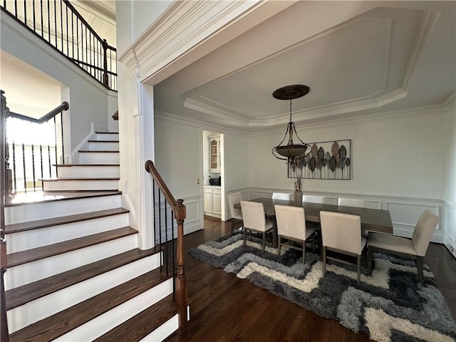 dining space featuring a tray ceiling, a wainscoted wall, dark wood-style floors, and stairway