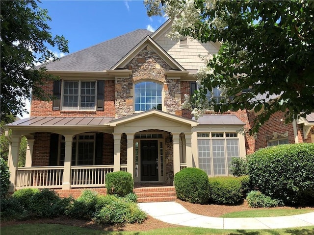 view of front of house featuring brick siding, stone siding, covered porch, and a standing seam roof