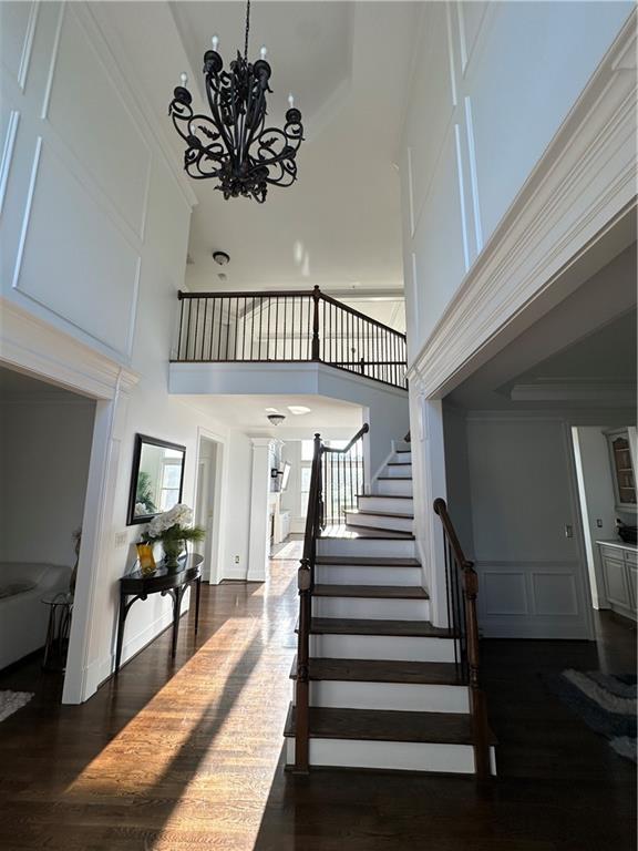 stairs featuring a chandelier, a decorative wall, ornamental molding, and wood finished floors