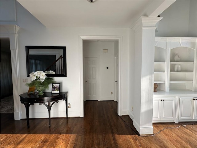 hallway with decorative columns, baseboards, and wood finished floors