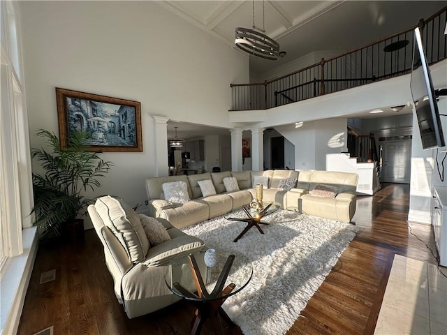 living room with coffered ceiling, wood finished floors, a towering ceiling, and ornate columns