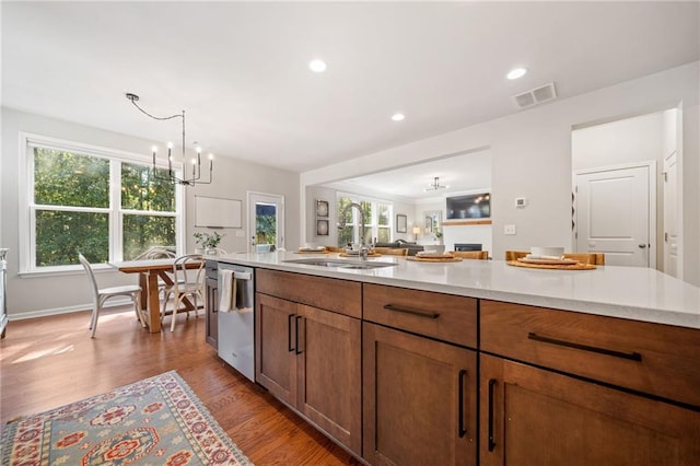 kitchen featuring sink, hanging light fixtures, stainless steel dishwasher, an inviting chandelier, and light hardwood / wood-style flooring