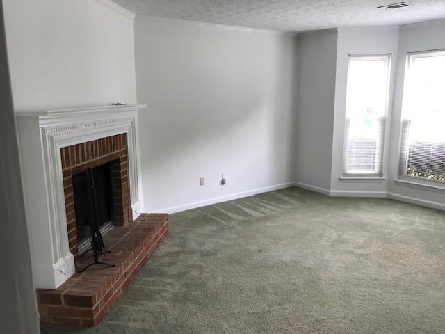 unfurnished living room with crown molding, carpet, a brick fireplace, and a textured ceiling