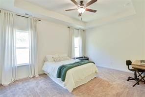 bedroom with a raised ceiling, ceiling fan, and light carpet