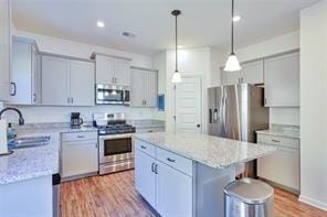 kitchen with appliances with stainless steel finishes, hanging light fixtures, a kitchen island, light hardwood / wood-style flooring, and sink