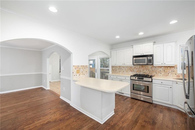 kitchen featuring appliances with stainless steel finishes, backsplash, white cabinets, dark hardwood / wood-style flooring, and kitchen peninsula