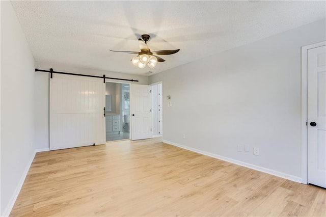 unfurnished bedroom with ensuite bathroom, a barn door, a textured ceiling, and light hardwood / wood-style flooring