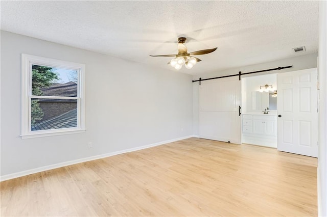 empty room with ceiling fan, a barn door, a textured ceiling, and light hardwood / wood-style flooring