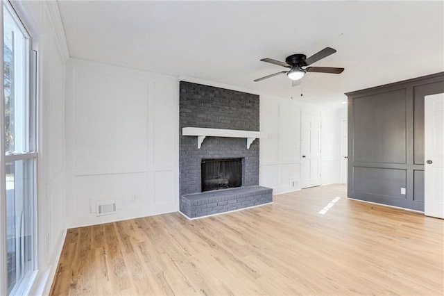 unfurnished living room with a brick fireplace, crown molding, ceiling fan, and light wood-type flooring