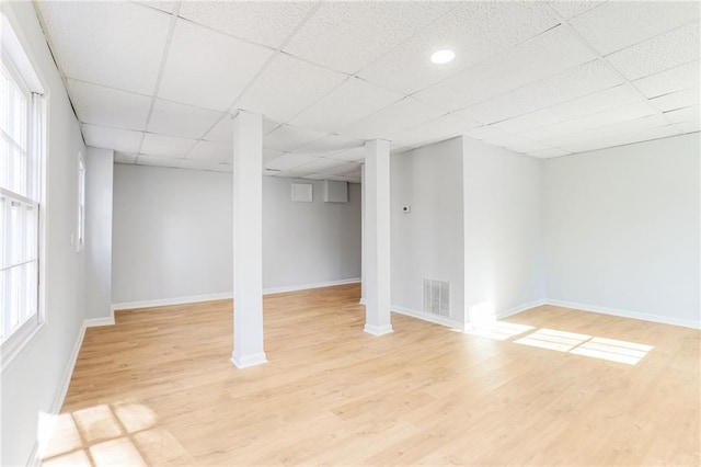 basement with a wealth of natural light, a paneled ceiling, and light hardwood / wood-style floors