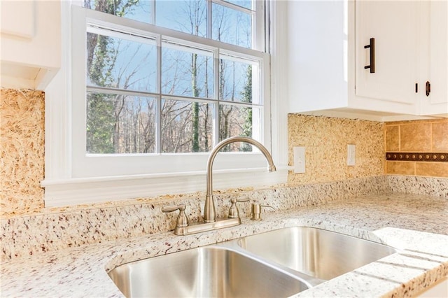 interior details featuring sink, white cabinets, and light stone counters