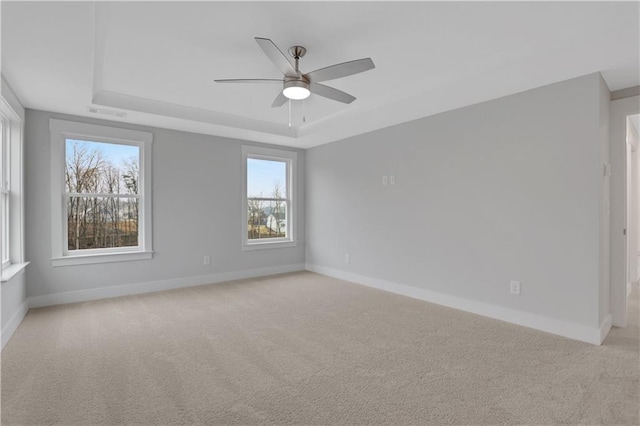 empty room featuring ceiling fan, light colored carpet, and a tray ceiling