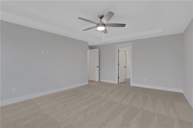 spare room with ceiling fan, light colored carpet, and a tray ceiling