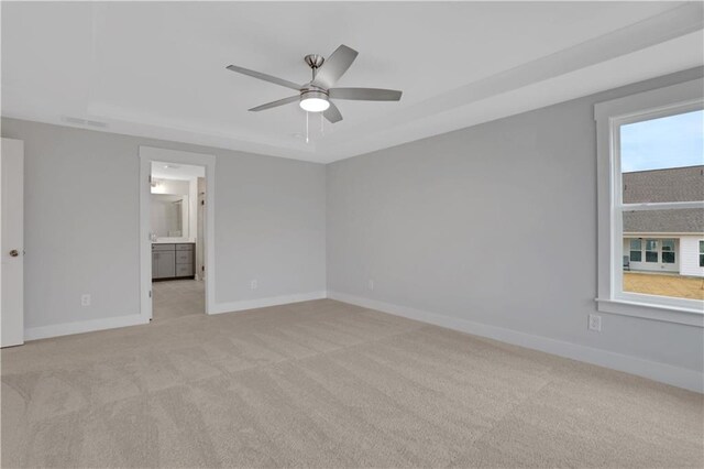 empty room featuring a raised ceiling, light carpet, and ceiling fan