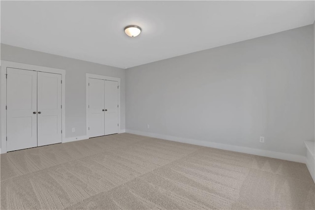 unfurnished bedroom featuring multiple closets and light carpet