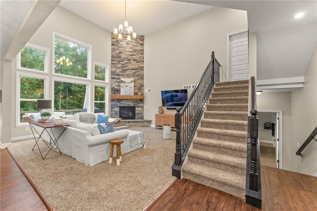 living room featuring a notable chandelier, a stone fireplace, wood-type flooring, and a high ceiling