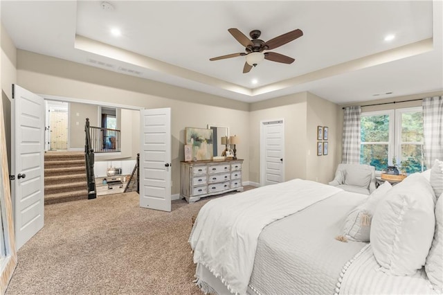 bedroom with light carpet, ceiling fan, and a tray ceiling