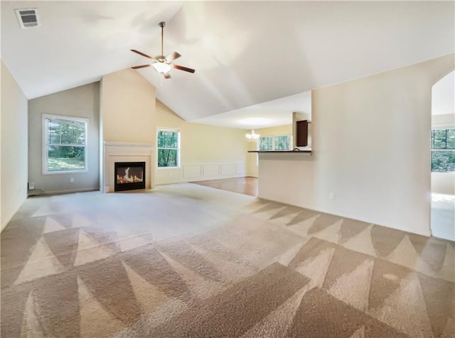 unfurnished living room featuring ceiling fan with notable chandelier, a healthy amount of sunlight, light colored carpet, and vaulted ceiling