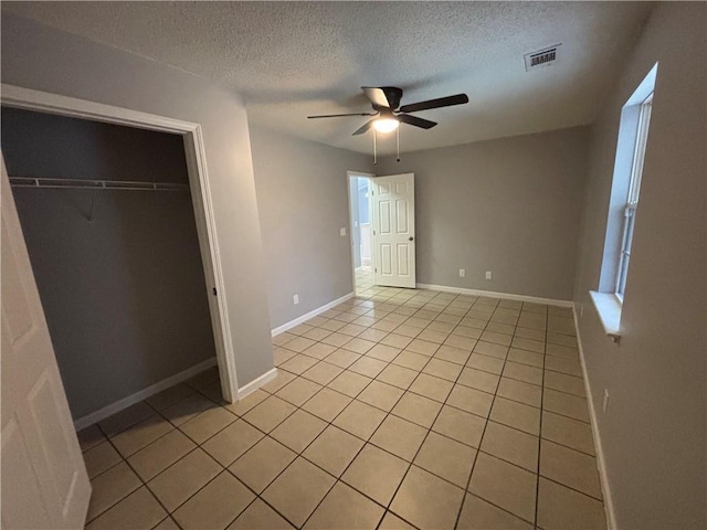 unfurnished bedroom featuring ceiling fan, light tile patterned floors, a textured ceiling, and a closet