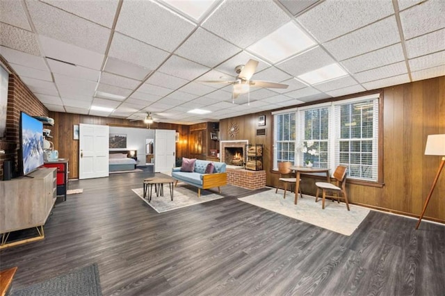 200 Mcguirts Bridge Rd, Covington, GA 30014 - living room featuring ceiling fan, wood walls, wood finished floors, a drop ceiling, and a brick fireplace