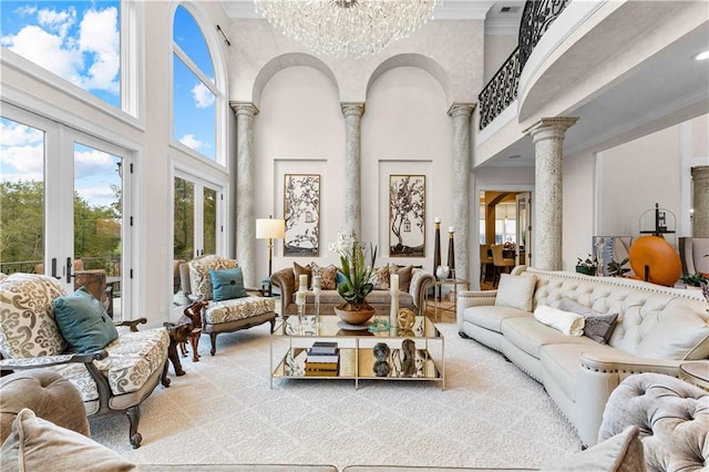 living room with french doors, a high ceiling, ornate columns, a chandelier, and ornamental molding