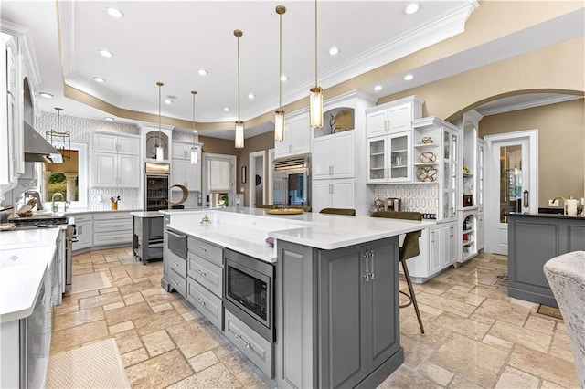 kitchen featuring gray cabinetry, a large island, decorative light fixtures, built in appliances, and a kitchen breakfast bar