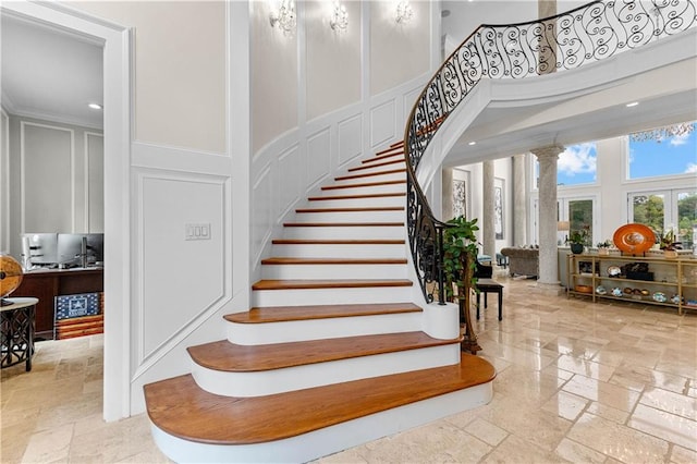 stairs featuring a high ceiling, crown molding, and ornate columns