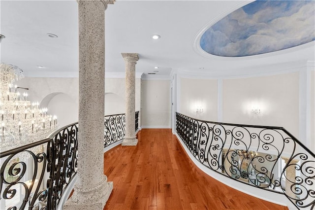 hallway featuring ornamental molding, hardwood / wood-style floors, ornate columns, and a chandelier