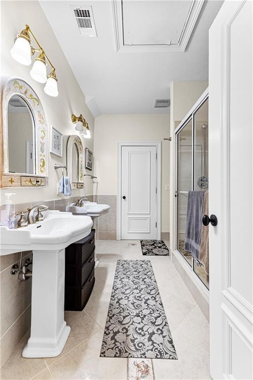 bathroom with dual sinks, tile patterned flooring, a shower with door, and tile walls