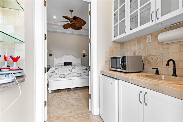 kitchen with ceiling fan, sink, decorative backsplash, ornamental molding, and white cabinets