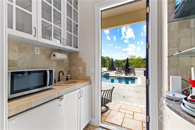 bar with backsplash, fridge, sink, and white cabinetry