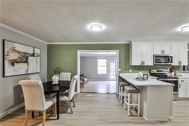 kitchen with a breakfast bar area, stainless steel appliances, crown molding, and white cabinets