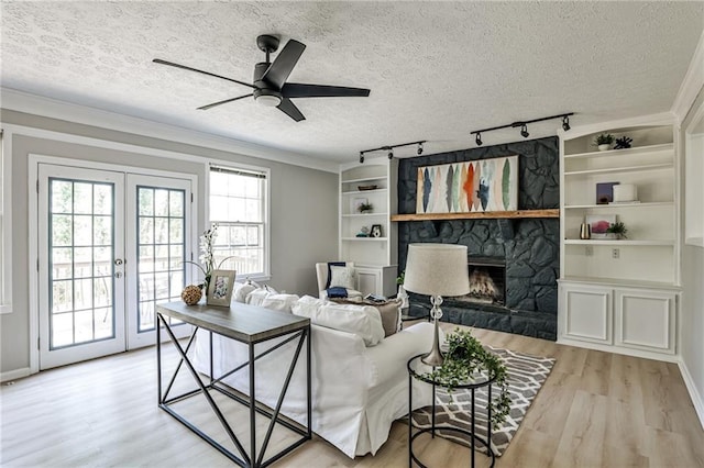 living area with ornamental molding, a fireplace, light wood-type flooring, a textured ceiling, and french doors