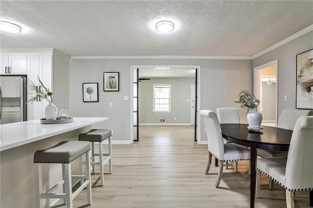 dining area featuring a textured ceiling, crown molding, visible vents, baseboards, and light wood finished floors