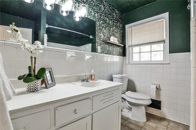 full bathroom with wallpapered walls, toilet, tile walls, tile patterned floors, and vanity