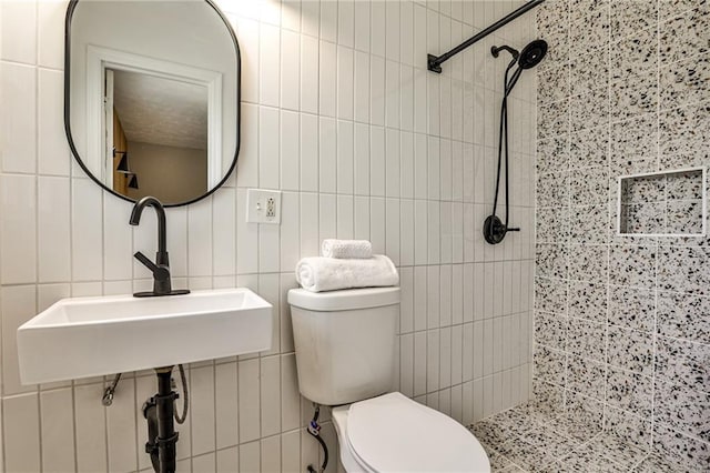 bathroom with tile walls, toilet, a tile shower, and a sink