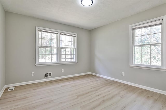 spare room featuring visible vents, plenty of natural light, and light wood-style floors