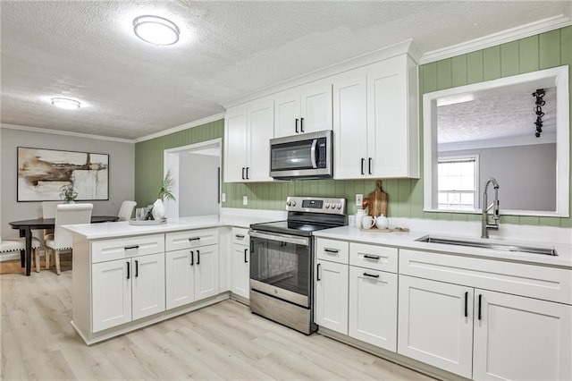 kitchen with light wood-style flooring, appliances with stainless steel finishes, a sink, a textured ceiling, and crown molding