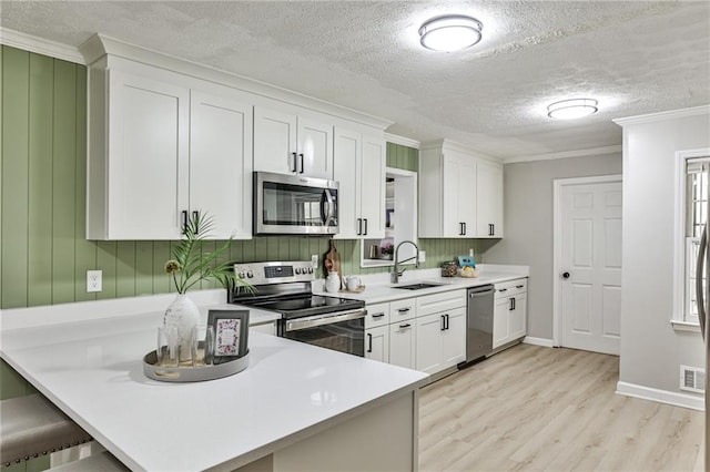 kitchen featuring a sink, light wood-style floors, crown molding, white cabinetry, and appliances with stainless steel finishes
