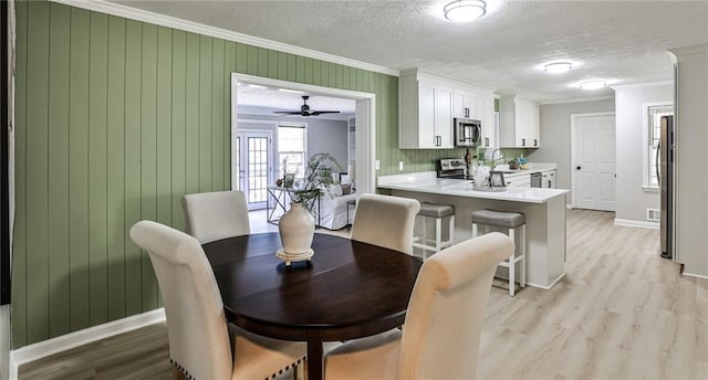 dining room with baseboards, ornamental molding, light wood-style floors, and a textured ceiling