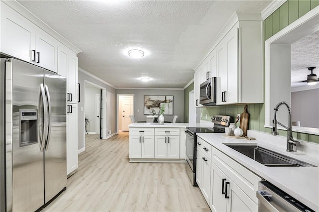 kitchen featuring a textured ceiling, white cabinets, a sink, stainless steel appliances, and a peninsula