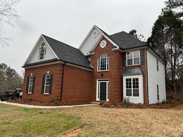 view of front facade with brick siding, a shingled roof, and a front yard