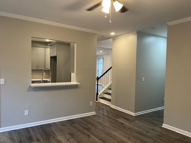 unfurnished living room featuring dark wood finished floors, crown molding, a brick fireplace, ceiling fan, and baseboards