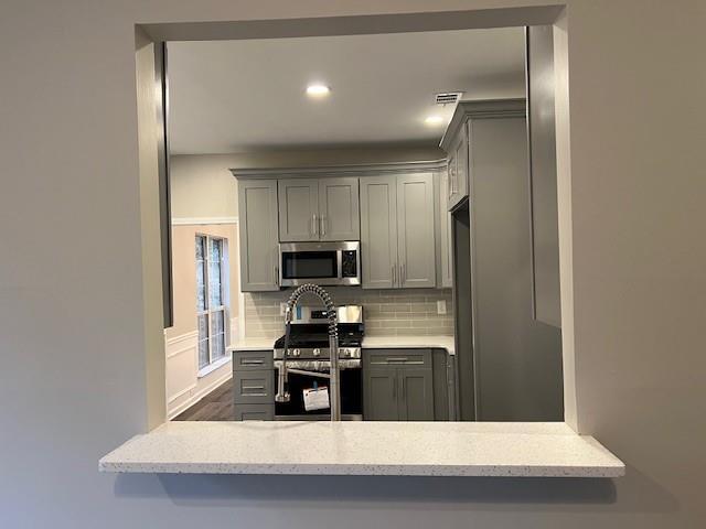 kitchen featuring recessed lighting, gray cabinetry, stainless steel appliances, a peninsula, and decorative backsplash