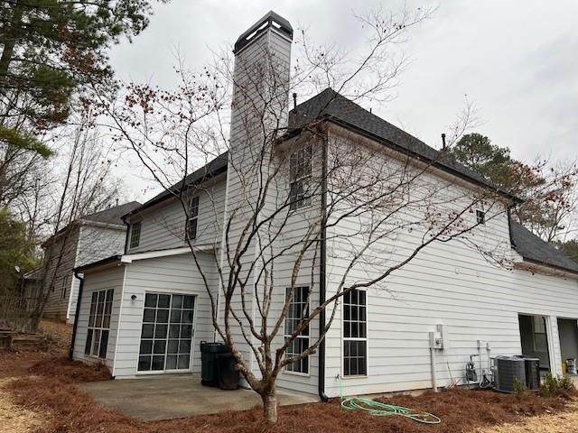 rear view of property with central air condition unit, a chimney, and a patio