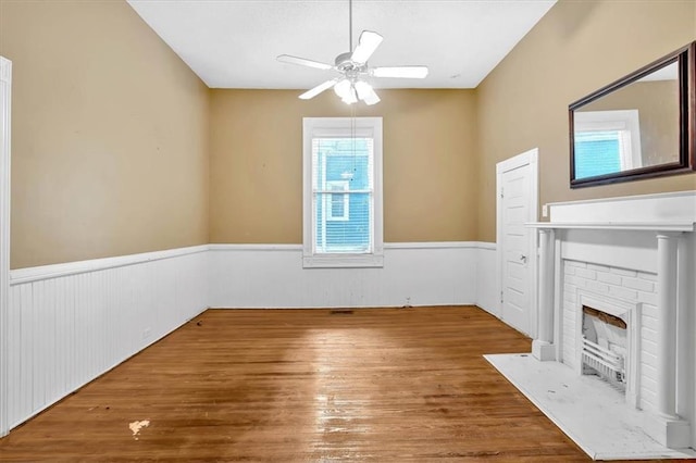 226 Noyes St, Cedartown, GA 30125 - unfurnished living room with wainscoting, a ceiling fan, wood finished floors, and a brick fireplace