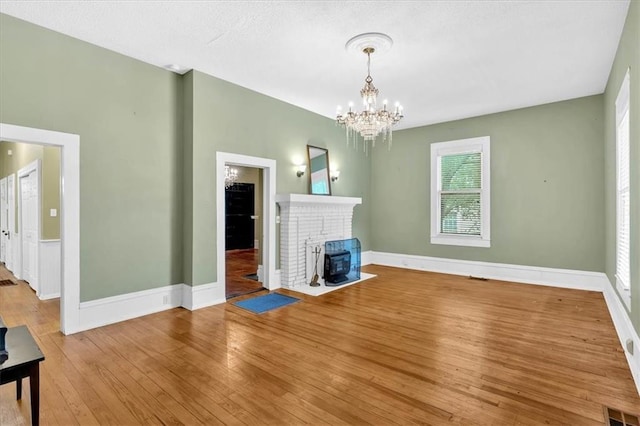 226 Noyes St, Cedartown, GA 30125 - unfurnished living room with wood-type flooring, a chandelier, a brick fireplace, and a textured ceiling
