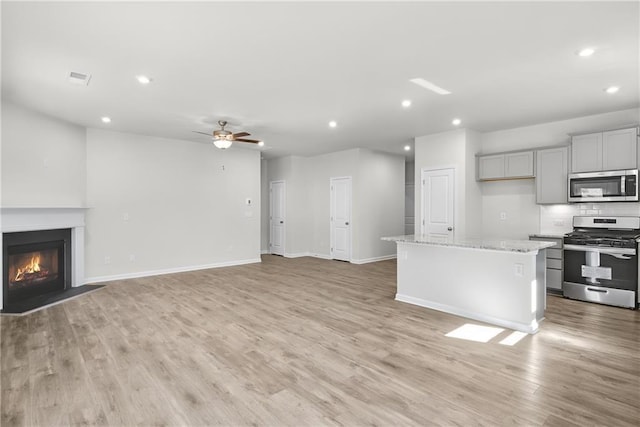 unfurnished living room with a glass covered fireplace, recessed lighting, light wood-style floors, baseboards, and ceiling fan